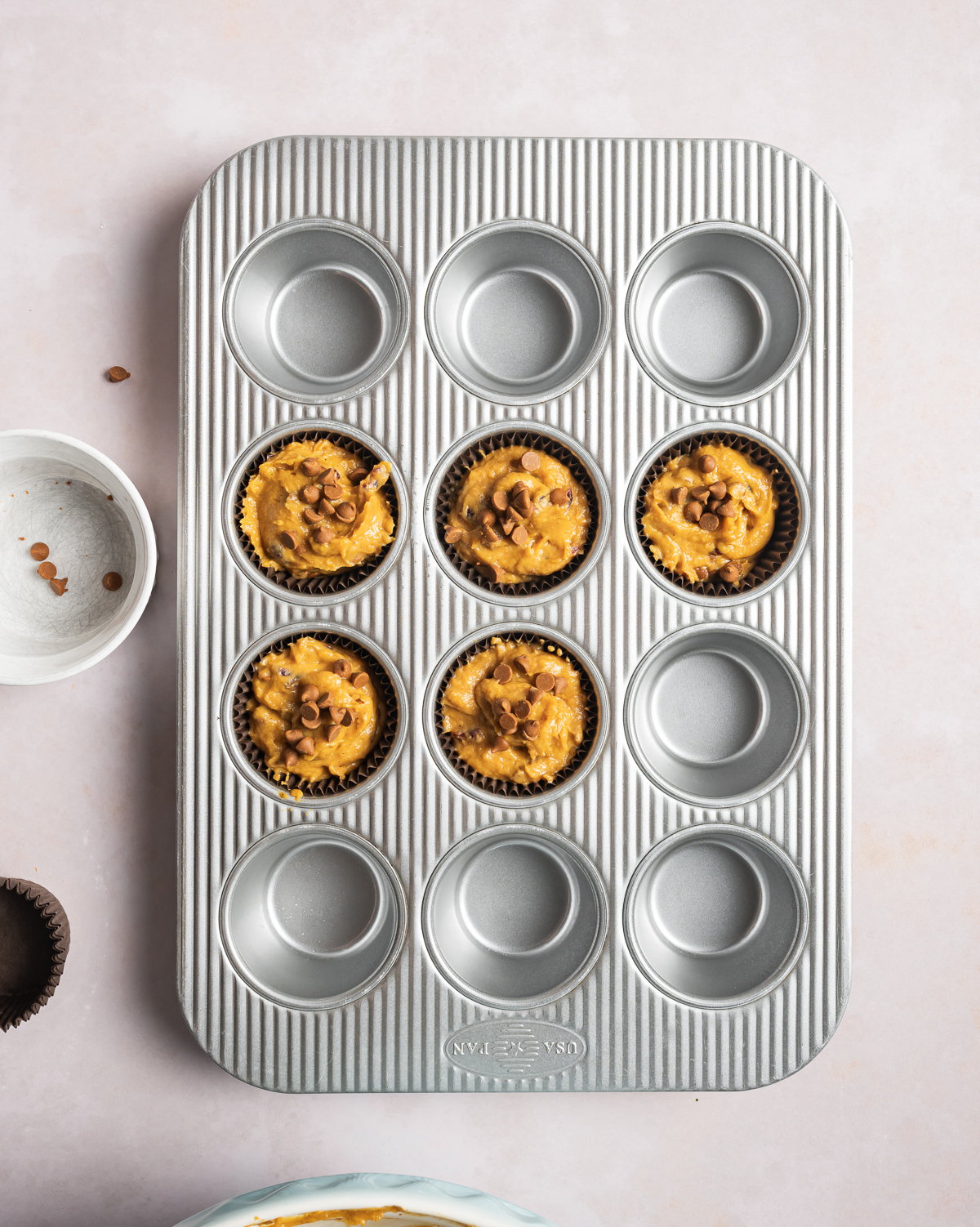 12 cup muffin tin with 5 holes filled with pumpkin muffin batter