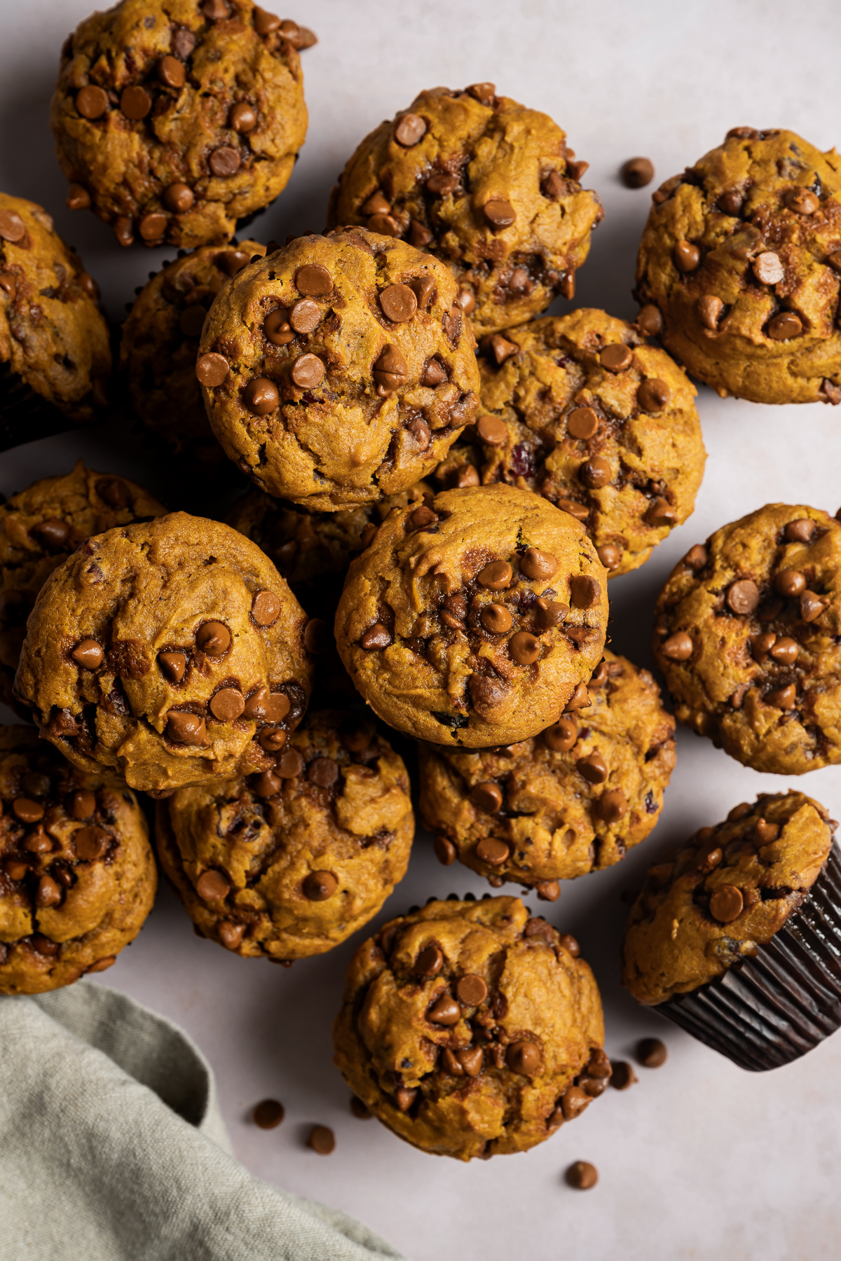 a pile of cinnamon pumpkin muffins in brown paper liners green napkin