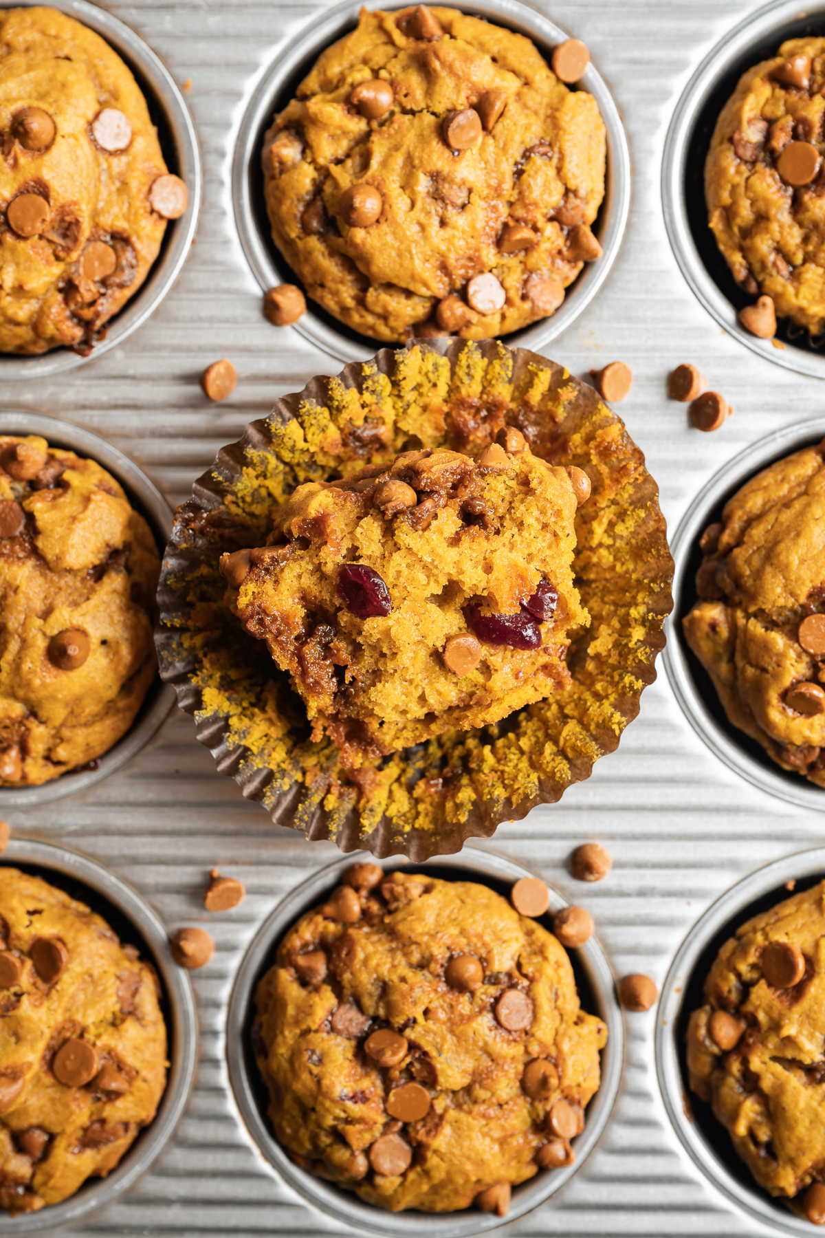 baked pumpkin muffins in a tin one cut in half unwrapped on top of a brown paper liner