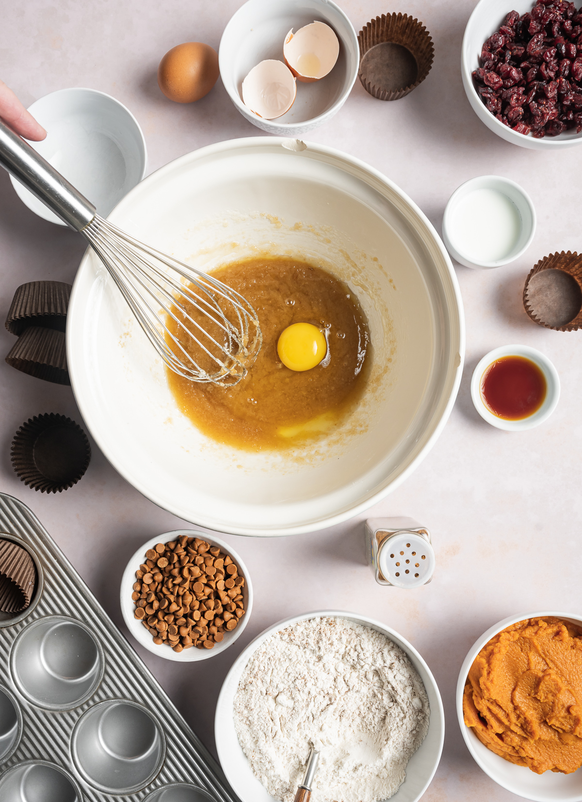 muffin batter with an egg in a bowl, various bowls of separate muffin ingredients