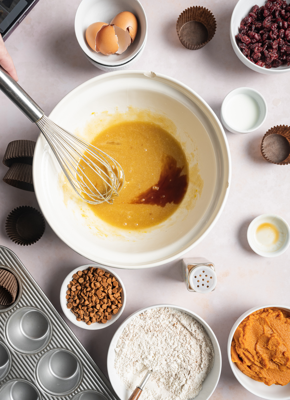 muffin batter being whisked in a bowl, various bowls of separate muffin ingredients