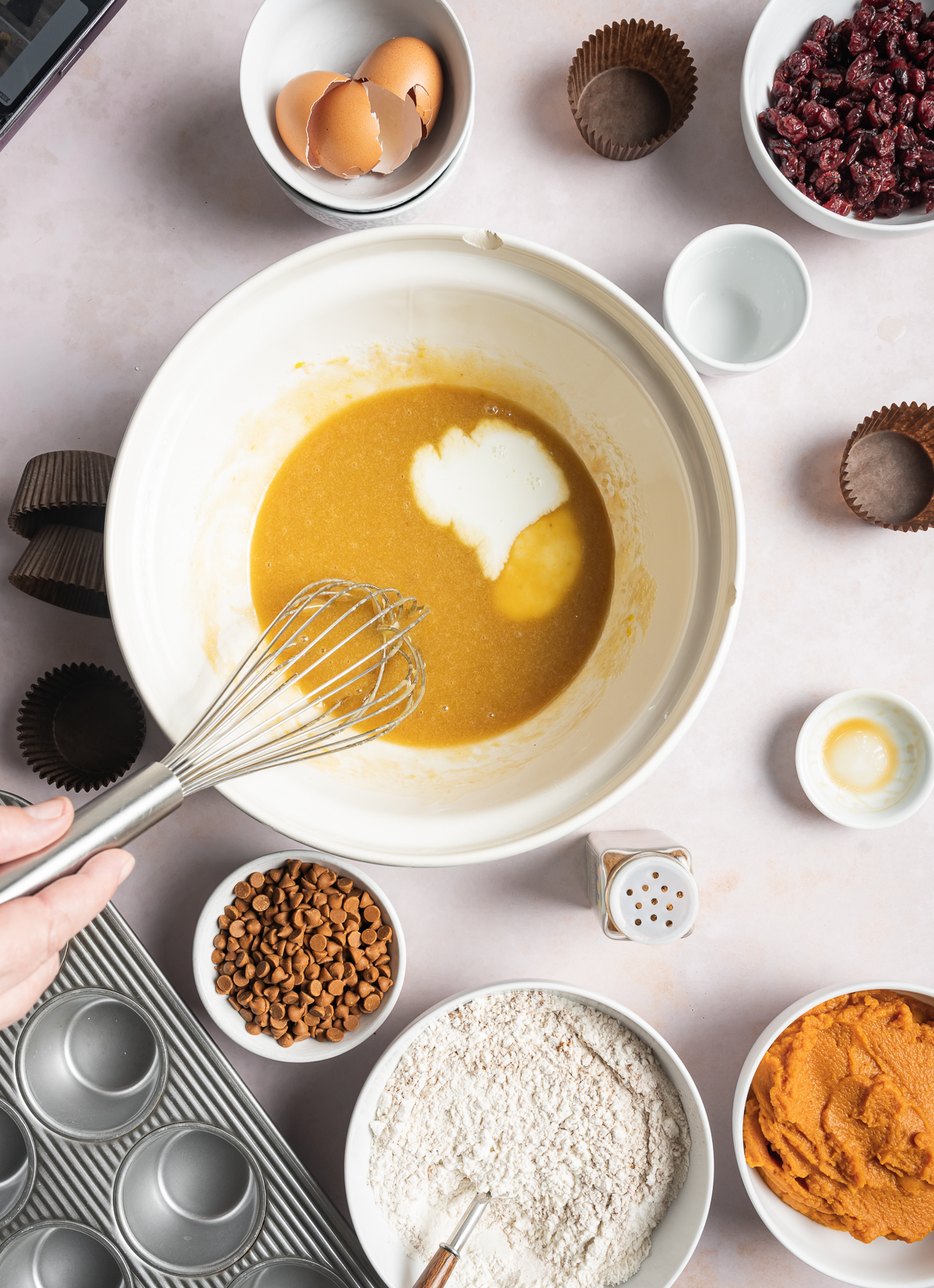 muffin batter being whisked in a bowl with milk, various bowls of separate muffin ingredients