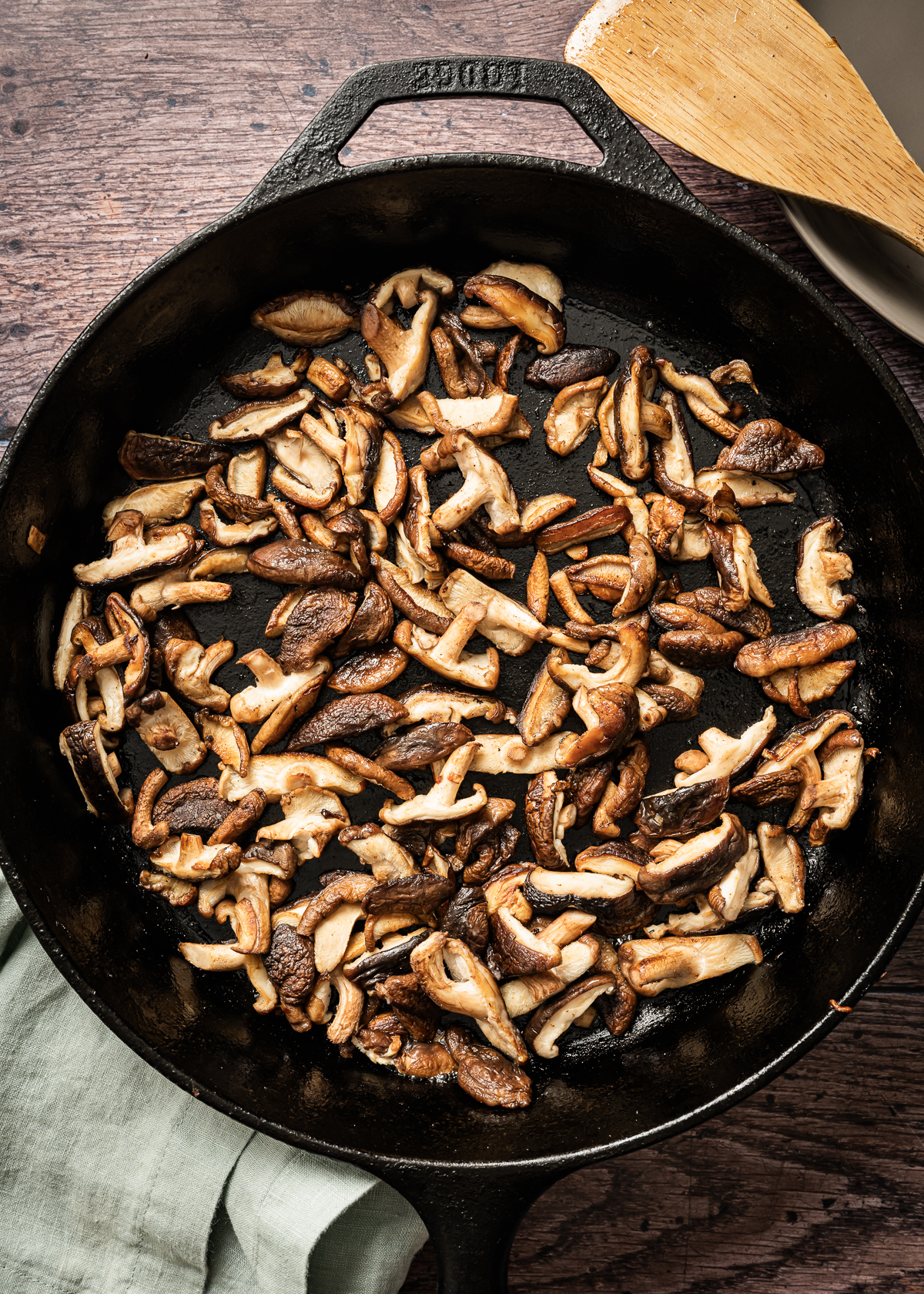 cooked shiitake mushrooms in cast iron pan bamboo spatula