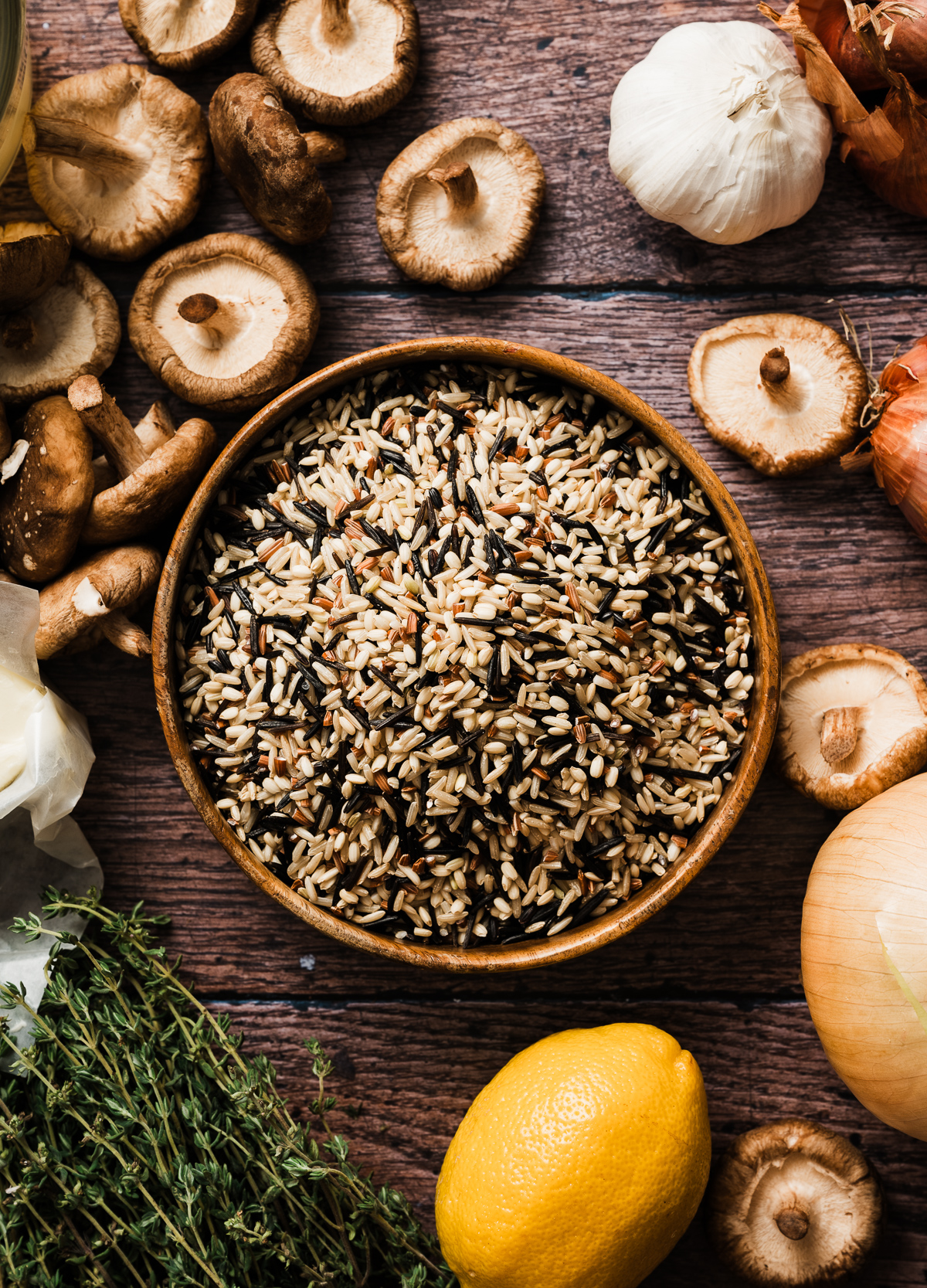 bowl of uncooked wild rice, shiitake mushroos garlic bulb whole yellow onion lemon fresh thyme