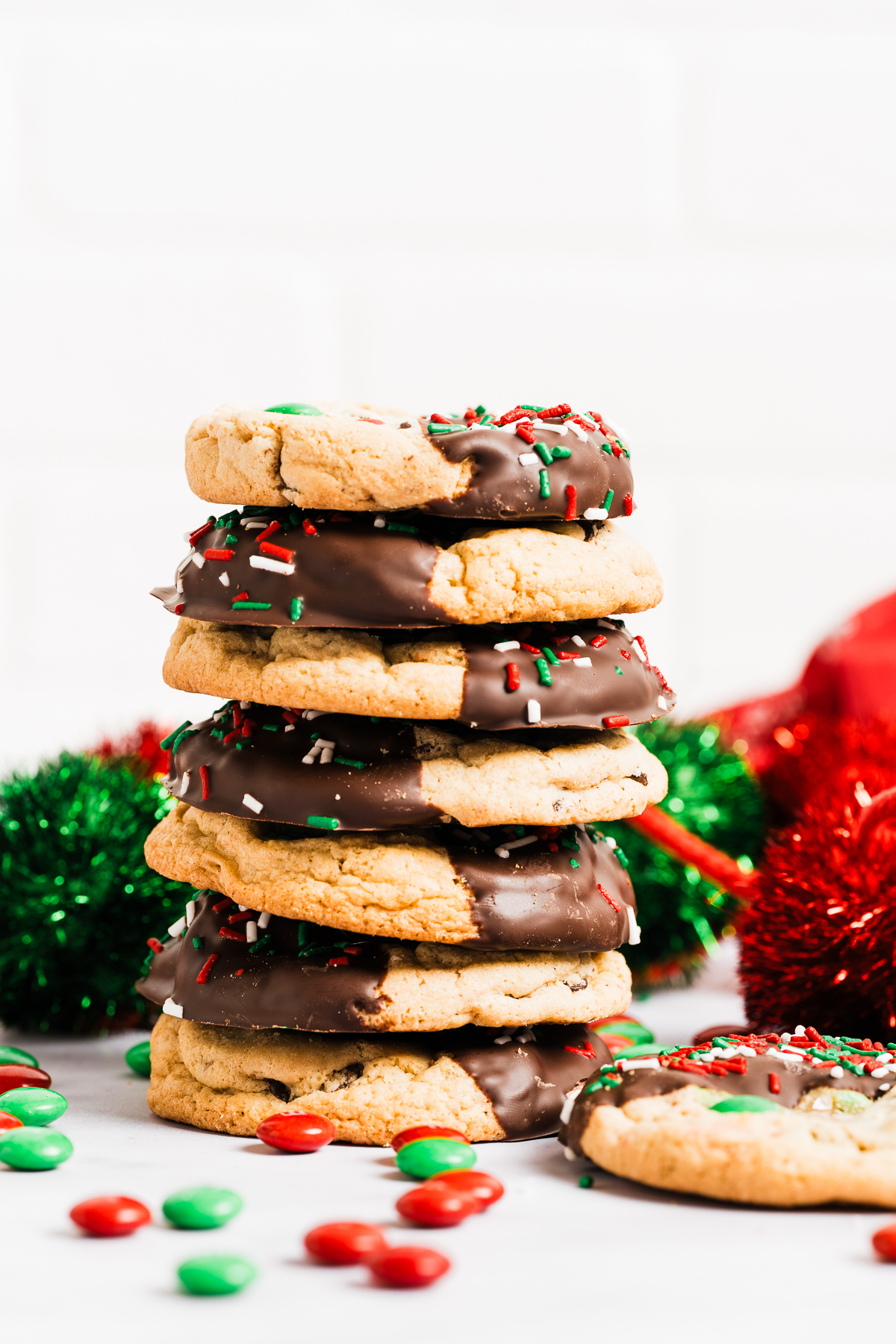 red and green M&M chewy chocolate chip cookies half dipped in chocolate decorated with red white and green sprinkles in a stack