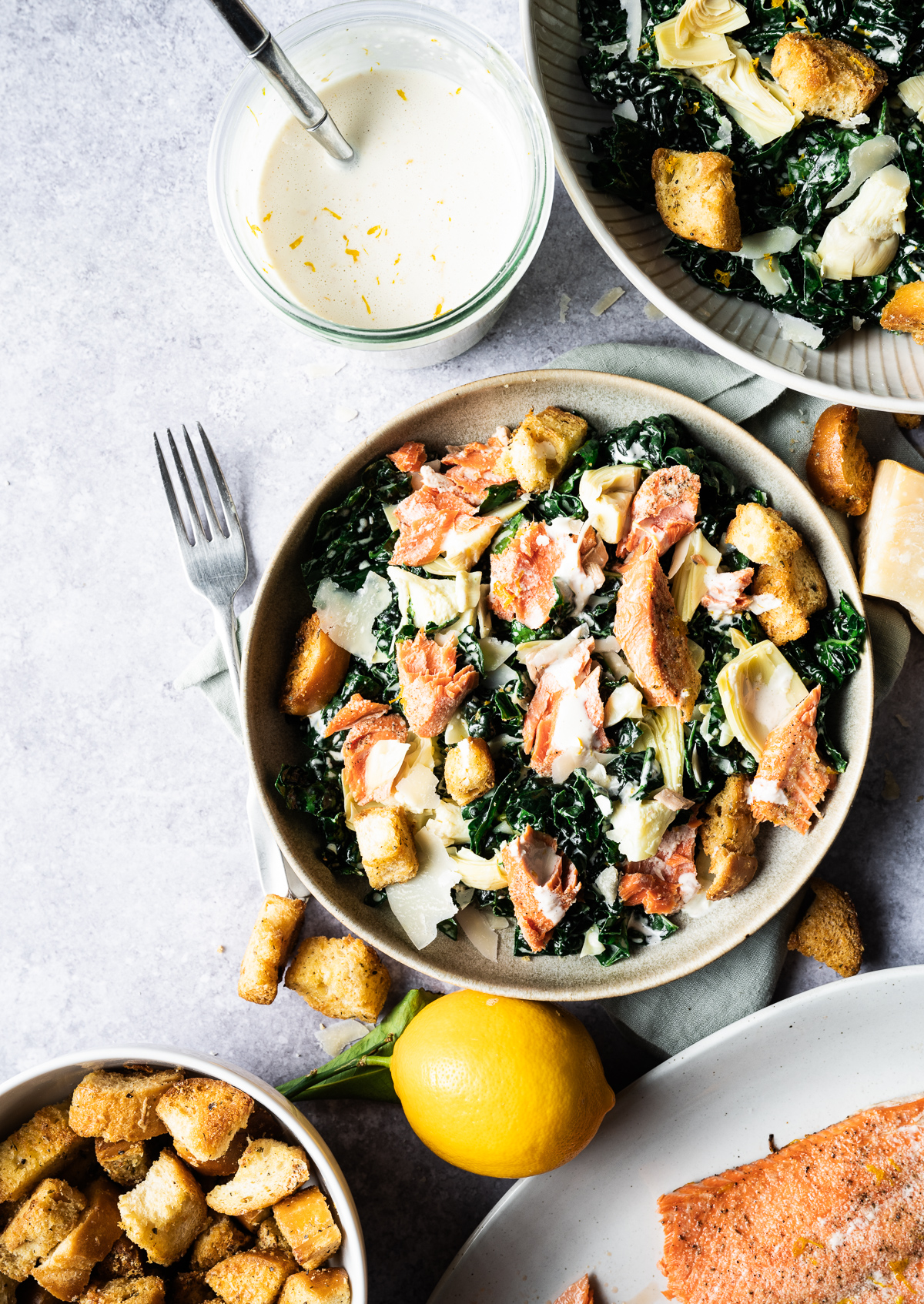 Salmon Caesar salads in bowls chunk of Parmesan cheese Meyer lemon jar of Meyer lemon Caesar dressing