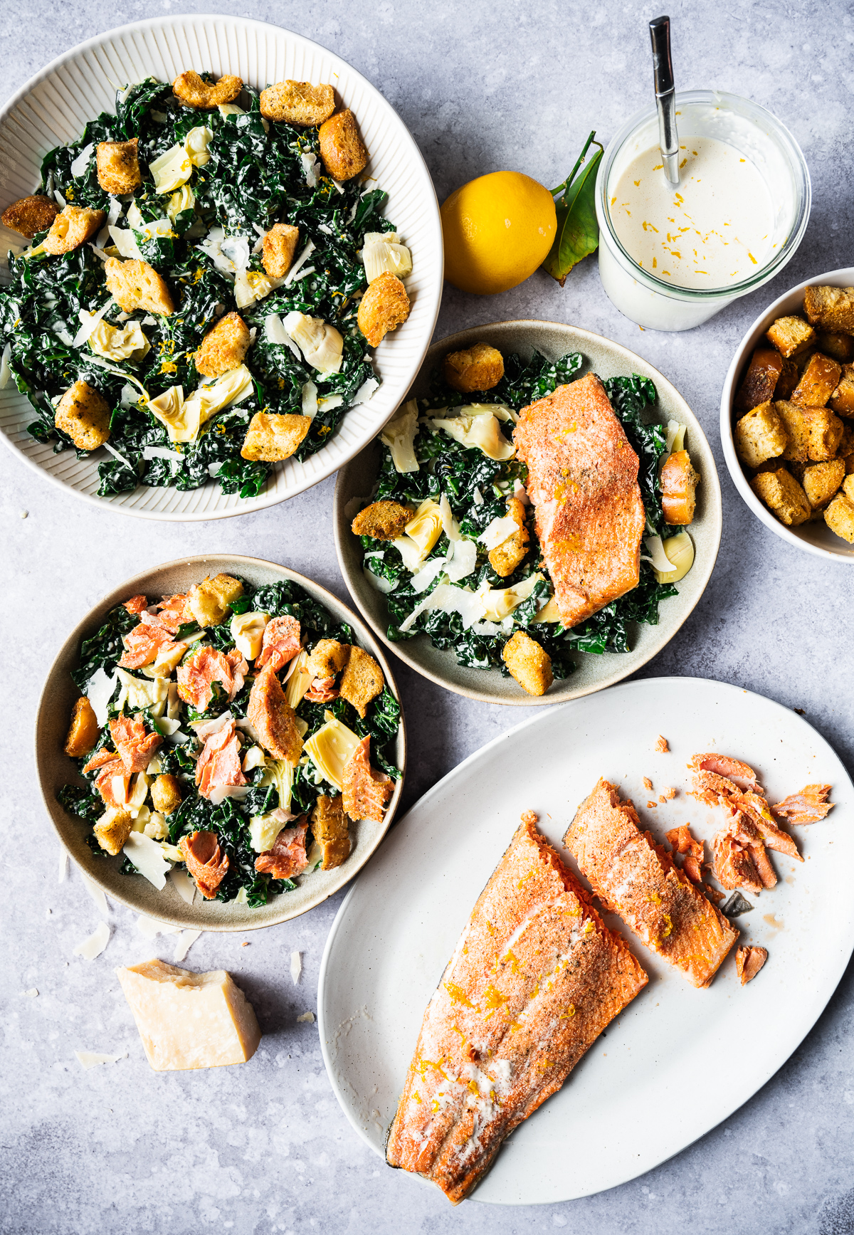 Salmon Caesar salads in bowls chunk of Parmesan cheese Meyer lemon jar of Meyer lemon Caesar dressing