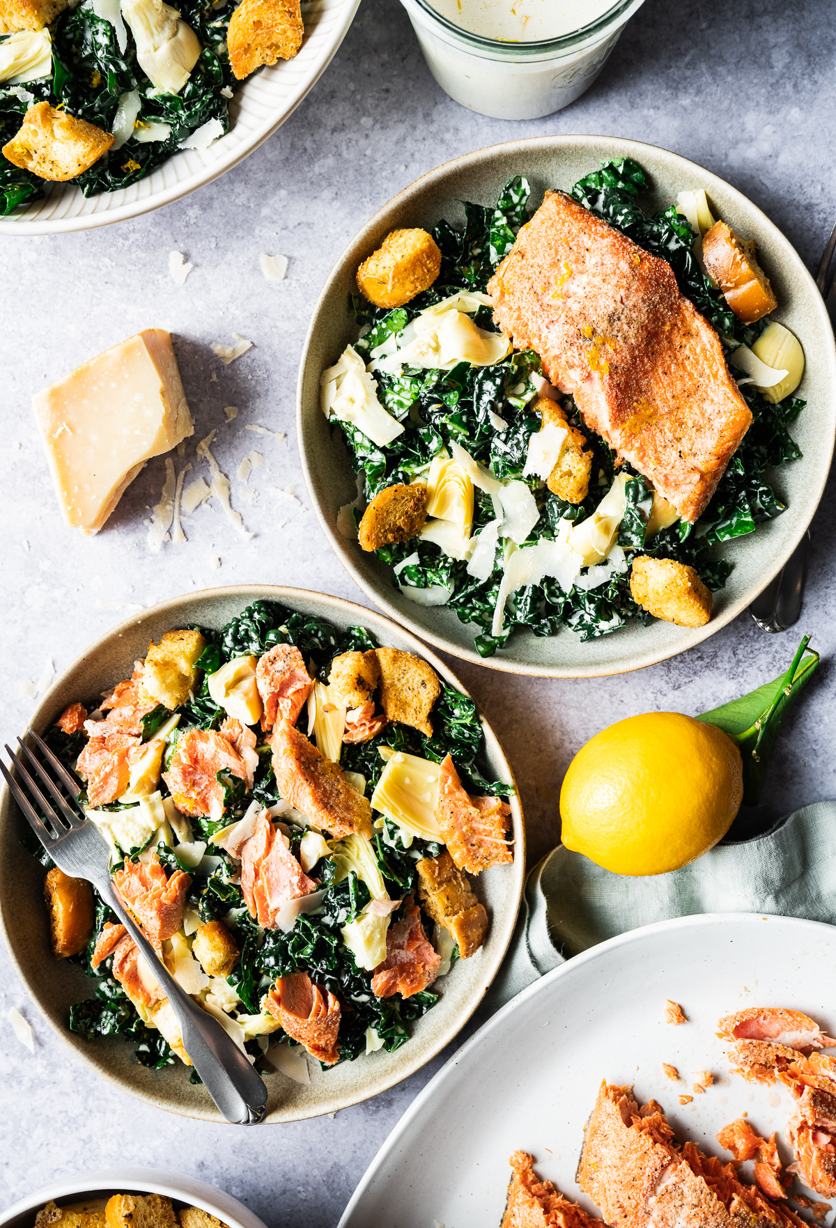 Salmon Caesar salads in bowls chunk of Parmesan cheese Meyer lemon jar of Meyer lemon Caesar dressing